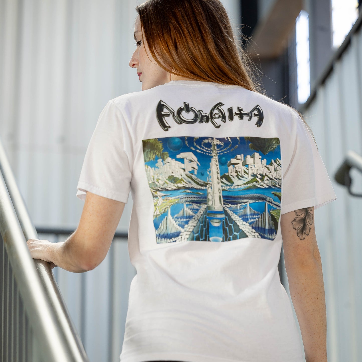 Woman wearing a white t-shirt with a colorful graphic and text, standing on a staircase.