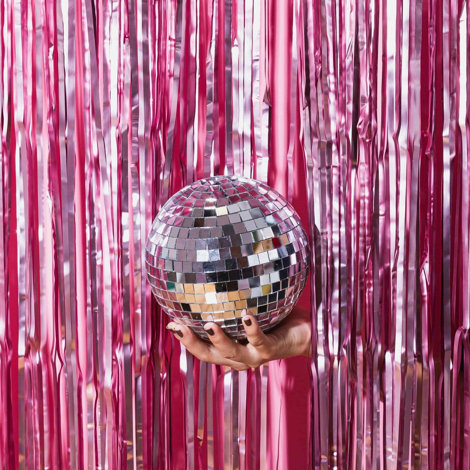 Hand holding a disco ball in front of pink tinsel curtains